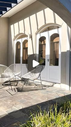 two white chairs sitting on top of a patio next to a building with an awning