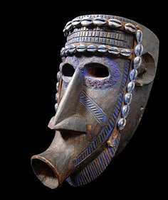 a wooden mask with chains and beads on it's face, against a black background