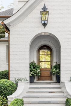 a white house with a brown door and two planters on the front steps next to it