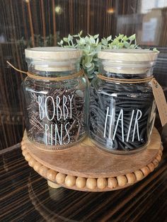 two jars with words on them sitting on a wooden stand next to a potted plant