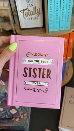 a person holding up a pink book with the words sister on it in front of bookshelves