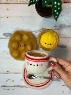 a hand holding a coffee cup next to two stuffed animals on a white wooden wall