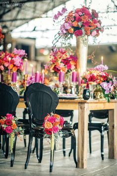 the table is set with black chairs and pink flowers on it, which are surrounded by candles