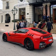 a red sports car parked in front of a building with people standing around it on the sidewalk