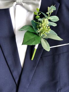 a boutonniere with green leaves and flowers on it's lapel