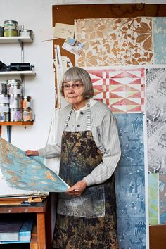 an older woman standing in front of a table holding a piece of art on it