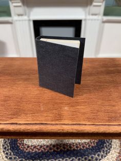 a small black book sitting on top of a wooden table next to a fire place