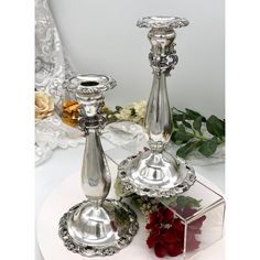 two silver candlesticks sitting on top of a white plate next to red flowers