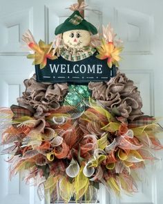 a welcome sign hanging from the front door with fall decorations around it and a scarecrow on top