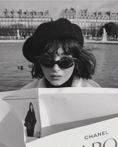 black and white photograph of a woman in sunglasses holding up a book that reads chanel d'or