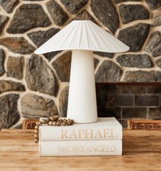 a lamp sitting on top of a book next to a stone wall and table in front of a fireplace