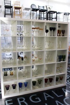 a display case filled with lots of wine glasses on top of white shelving units