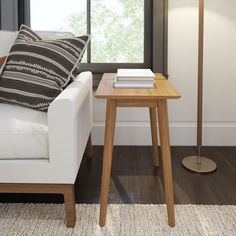 a white couch sitting next to a wooden table with books on it and a lamp