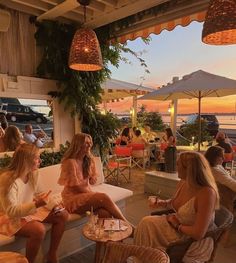 several women sitting at tables talking and having drinks in front of an ocean view restaurant