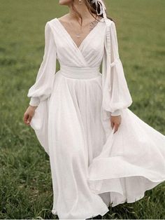 a woman in a white dress is walking through the grass with her hand on her hip