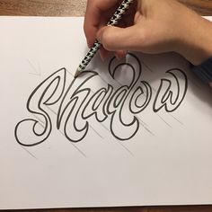 someone is writing the word shadow on paper with a marker and pencil in their hand