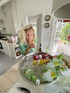 a woman standing in front of a large metal bowl filled with bottles and ice cubes