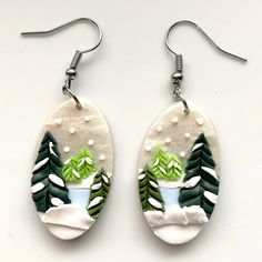 the earrings are decorated with green and white snowflakes, pine trees, and mountains