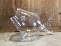 a clear glass fish sitting on top of a wooden table next to a wall mounted hook