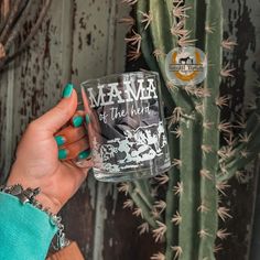 a woman holding up a glass with the words mama on it in front of a cactus