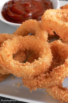 fried onion rings on a plate with ketchup and dipping sauce in the background