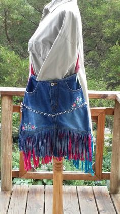 a woman's denim skirt with fringes and beads on the bottom is standing on a wooden deck