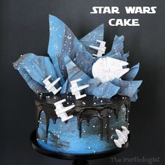 a star wars cake decorated with blue frosting and white icing, on top of a black stand