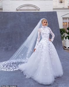 a woman in a wedding dress with a veil on her head and flowers on the skirt