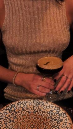 a woman is holding a drink in her hand while sitting at a table with plates on it