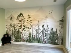 a bear sitting on the floor in front of a wall with trees painted on it