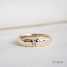 a gold wedding ring with a diamond set in the center on a white cloth background