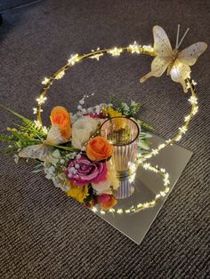 an arrangement of flowers and lights on the floor with a butterfly sitting on top of it