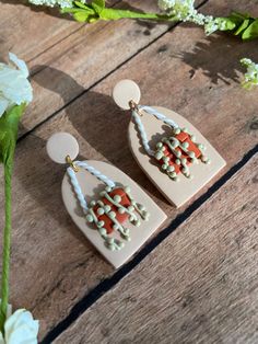 a pair of white earrings with orange and green beads on them sitting next to flowers