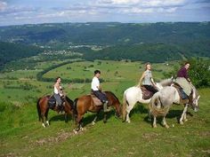 four people riding horses on top of a grassy hill with rolling hills in the background