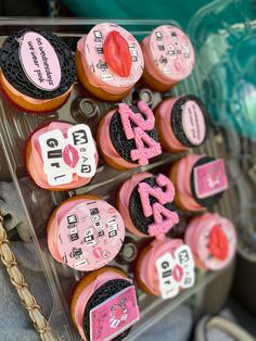 cupcakes decorated with pink and black icing are displayed in a plastic container