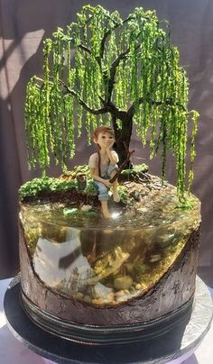 a cake with a boy sitting on top of it and a tree in the background