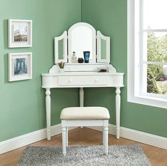 a white dressing table with a mirror and stool in front of green walls, along with pictures on the wall