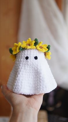 a hand holding a small white object with yellow flowers on it's head and eyes