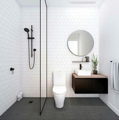 a modern bathroom with black and white tiles on the floor, toilet, shower head, sink, mirror and towel rack