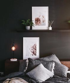 a bed with two pictures on the wall above it and some plants in vases