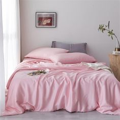 a bed with pink sheets and pillows in a room next to a potted plant