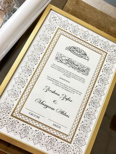 an ornate wedding card with gold border and calligraphy on the inside is displayed in front of a white bat