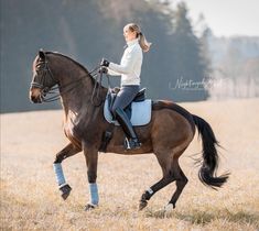 a young woman riding on the back of a brown horse in a field with tall grass