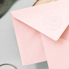 a pink envelope with a rose cut out on the front and an open ring next to it