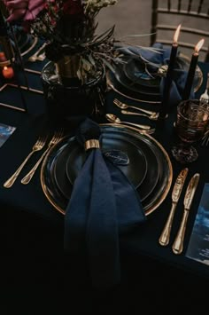 the table is set with black and gold plates, silverware, and napkins