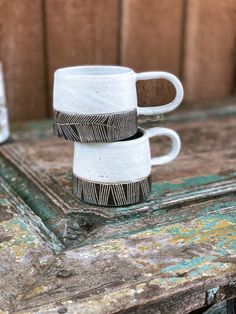 two white coffee mugs stacked on top of each other in front of a wooden door