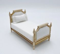 a small bed with white linens and gold trim on the headboard is shown