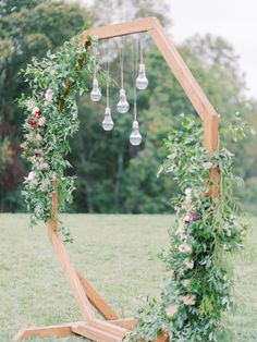 a wooden arch decorated with greenery and hanging lightbulbs for an outdoor ceremony