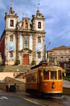 an orange trolley car traveling down a street next to a tall building with two towers