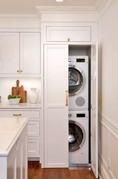 a washer and dryer in a white kitchen with wood flooring, built - in cabinets